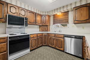 Kitchen featuring light countertops, stainless steel dishwasher, black microwave, light floors, and brown cabinets