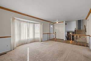 Unfurnished living room with carpet, stairway, a textured ceiling, and crown molding