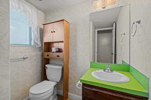 Bathroom featuring a textured ceiling, wallpapered walls, and vanity