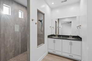 Full bathroom with double vanity, a walk in shower, and light wood-style floors