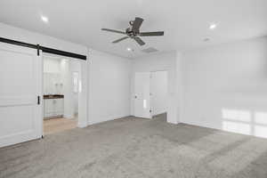 Unfurnished bedroom featuring a barn door, light colored carpet, recessed lighting, a ceiling fan, and ensuite bathroom