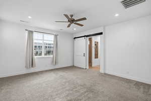 Unfurnished bedroom featuring a barn door, light carpet, ceiling fan, recessed lighting, and connected bathroom