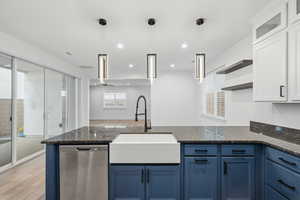 Kitchen with blue cabinetry, light wood-style floors, dishwasher, dark stone countertops, and decorative light fixtures