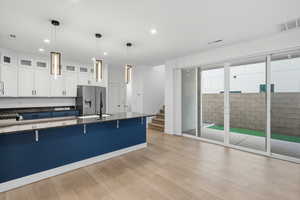 Kitchen featuring white cabinetry, dark stone countertops, a kitchen breakfast bar, pendant lighting, and light wood-style floors