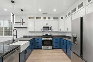 Kitchen featuring white cabinetry, blue cabinetry, stainless steel appliances, glass insert cabinets, and recessed lighting