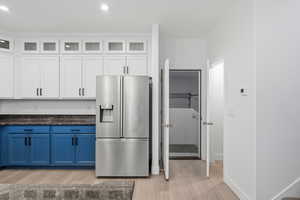 Kitchen featuring blue cabinets, stainless steel refrigerator with ice dispenser, white cabinetry, glass insert cabinets, and light wood-style flooring