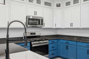 Kitchen with blue cabinetry, appliances with stainless steel finishes, white cabinetry, and glass insert cabinets