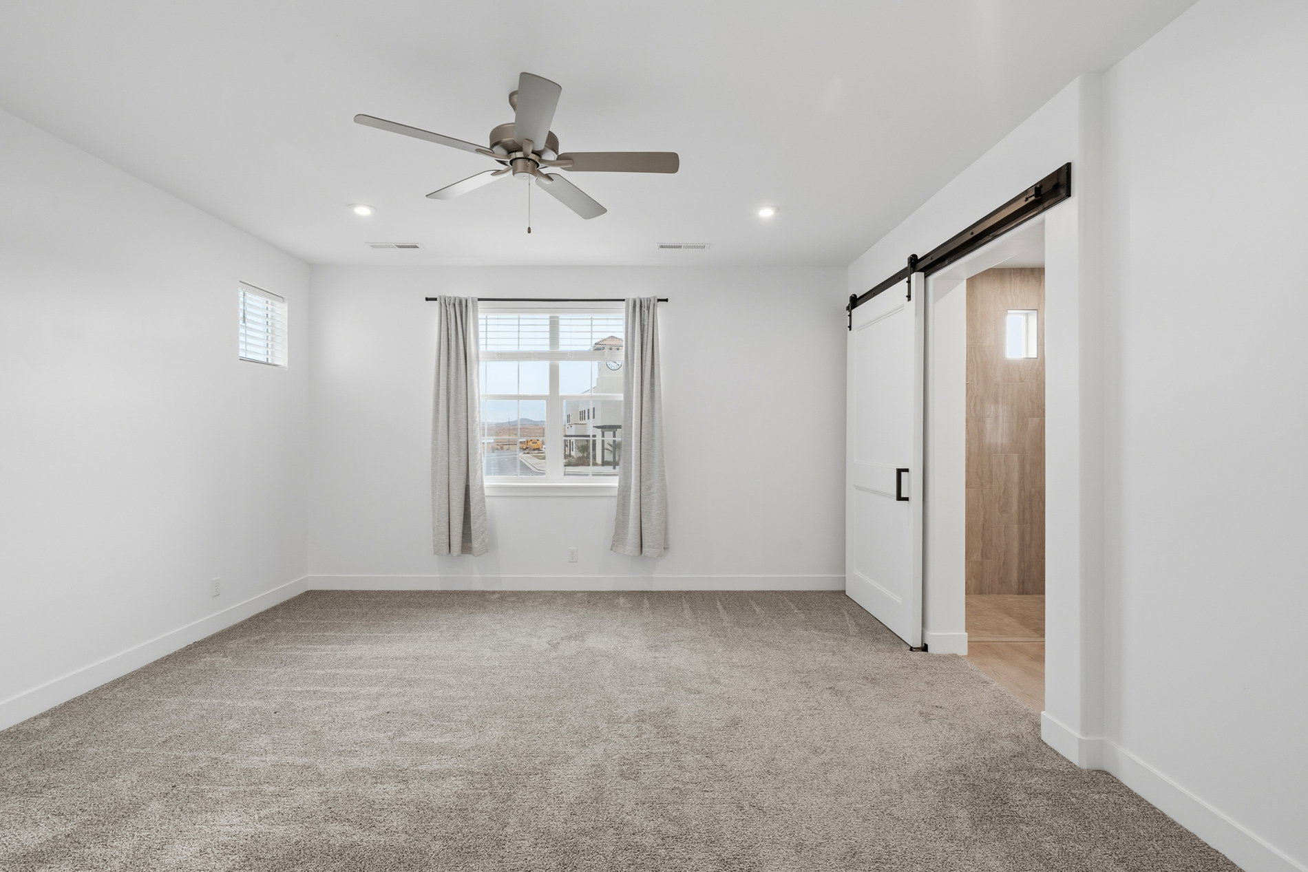 Empty room with light carpet, a barn door, ceiling fan, and recessed lighting