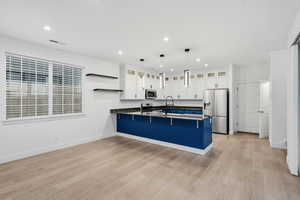 Kitchen featuring open shelves, white cabinetry, a peninsula, stainless steel appliances, and a breakfast bar