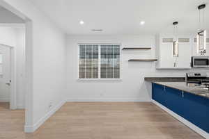 Kitchen with dark stone countertops, white cabinets, open shelves, light wood-type flooring, and glass insert cabinets