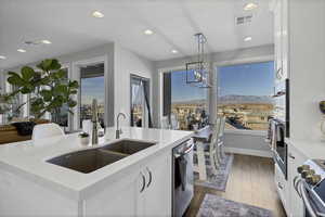 Kitchen with white cabinets, hanging light fixtures, appliances with stainless steel finishes, dark wood-style floors, and a center island with sink