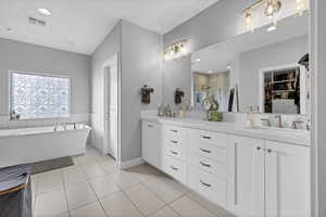 Bathroom with double vanity, a soaking tub, a spacious closet, light tile patterned floors, and recessed lighting