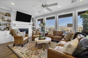 Living room with a glass covered fireplace, ceiling fan, wood finished floors, built in shelves, and recessed lighting