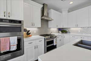 Kitchen featuring appliances with stainless steel finishes, white cabinets, wall chimney range hood, and recessed lighting