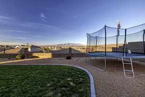 View of playground featuring a trampoline, a fenced backyard, and a mountain view