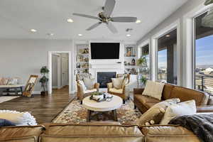 Living area with built in features, a glass covered fireplace, wood finished floors, a ceiling fan, and recessed lighting