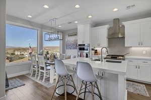 Kitchen with white cabinetry, wall chimney exhaust hood, light wood finished floors, pendant lighting, and recessed lighting
