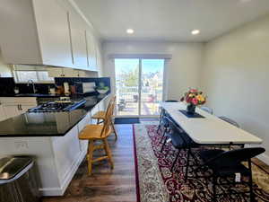 Kitchen with a kitchen bar, dark wood-style floors, white cabinetry, dark stone counters, and recessed lighting
