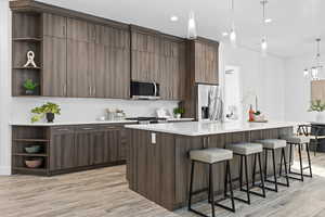 Kitchen with open shelves, decorative light fixtures, wood tiled floors, a kitchen island with sink, and a breakfast bar area