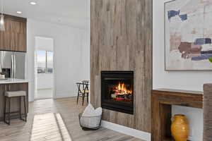 Detailed view of stainless steel fridge with ice dispenser, wood finished floors, a lit fireplace, and recessed lighting