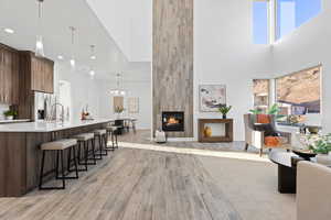 Living room featuring light wood-style floors, a large fireplace, a high ceiling, and a chandelier
