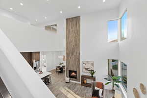 Living room with recessed lighting, light wood-style floors, a large fireplace, healthy amount of natural light, and a high ceiling