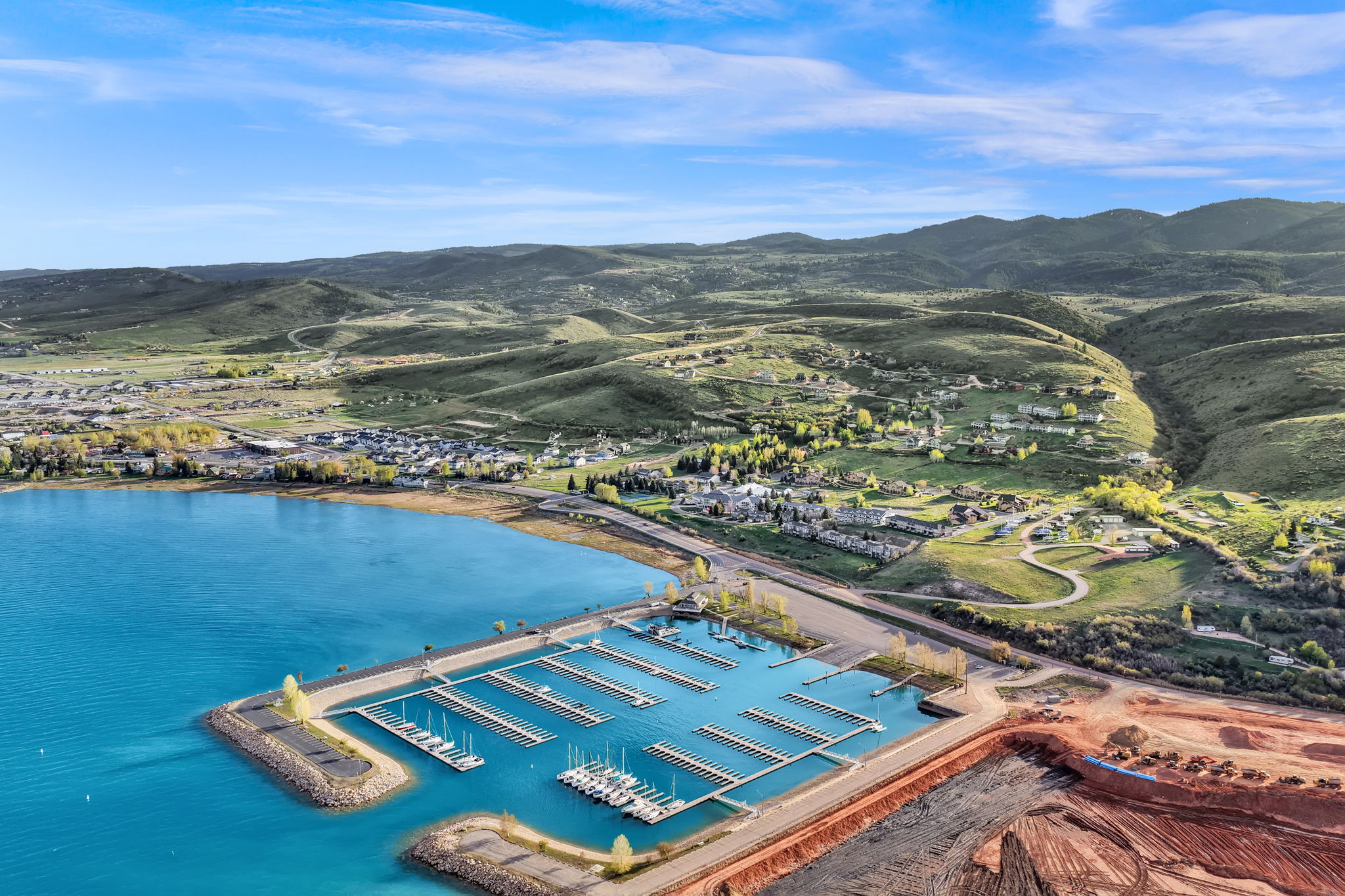 Marina with multiple boat slips and a breakwater, set against a backdrop of rolling green hills and distant mountains