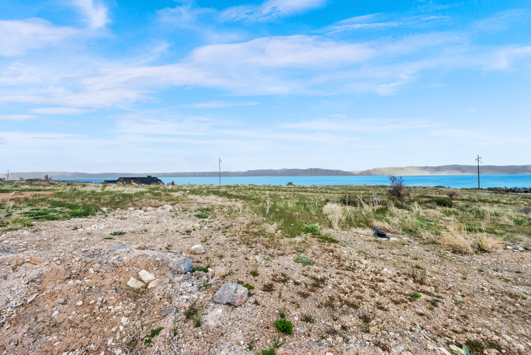 Expansive land parcel featuring natural ground cover, distant water body, and distant hills