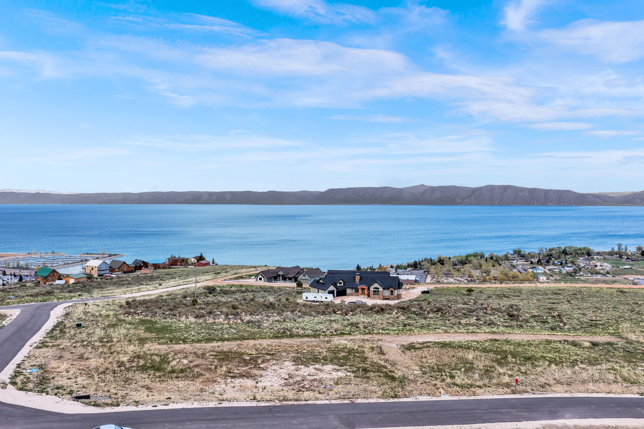 Expansive property with a large body of water, distant mountains, a partially constructed residence, and paved roads