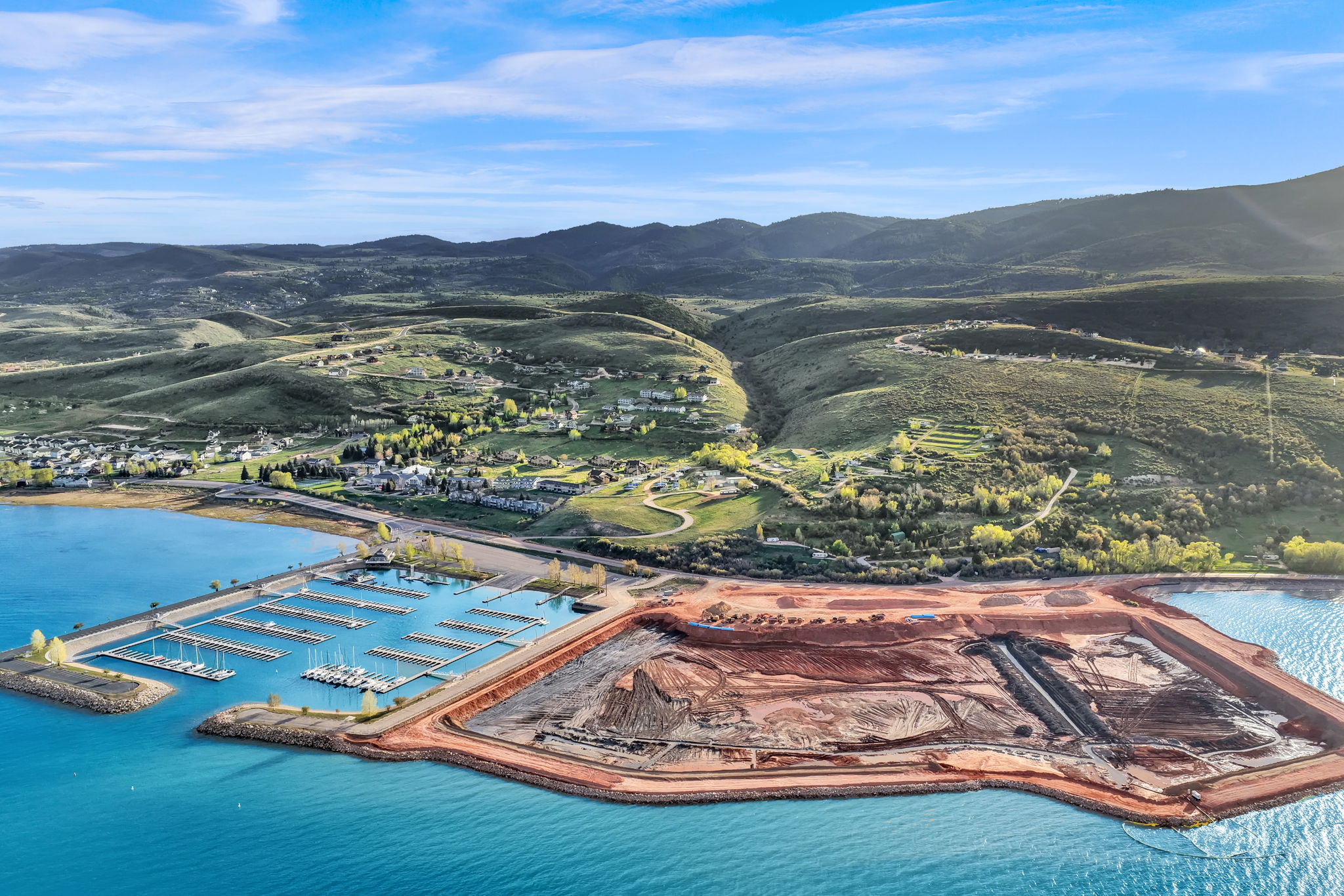Expansive waterfront property featuring a marina with multiple boat slips, turquoise water, and an adjacent land development area