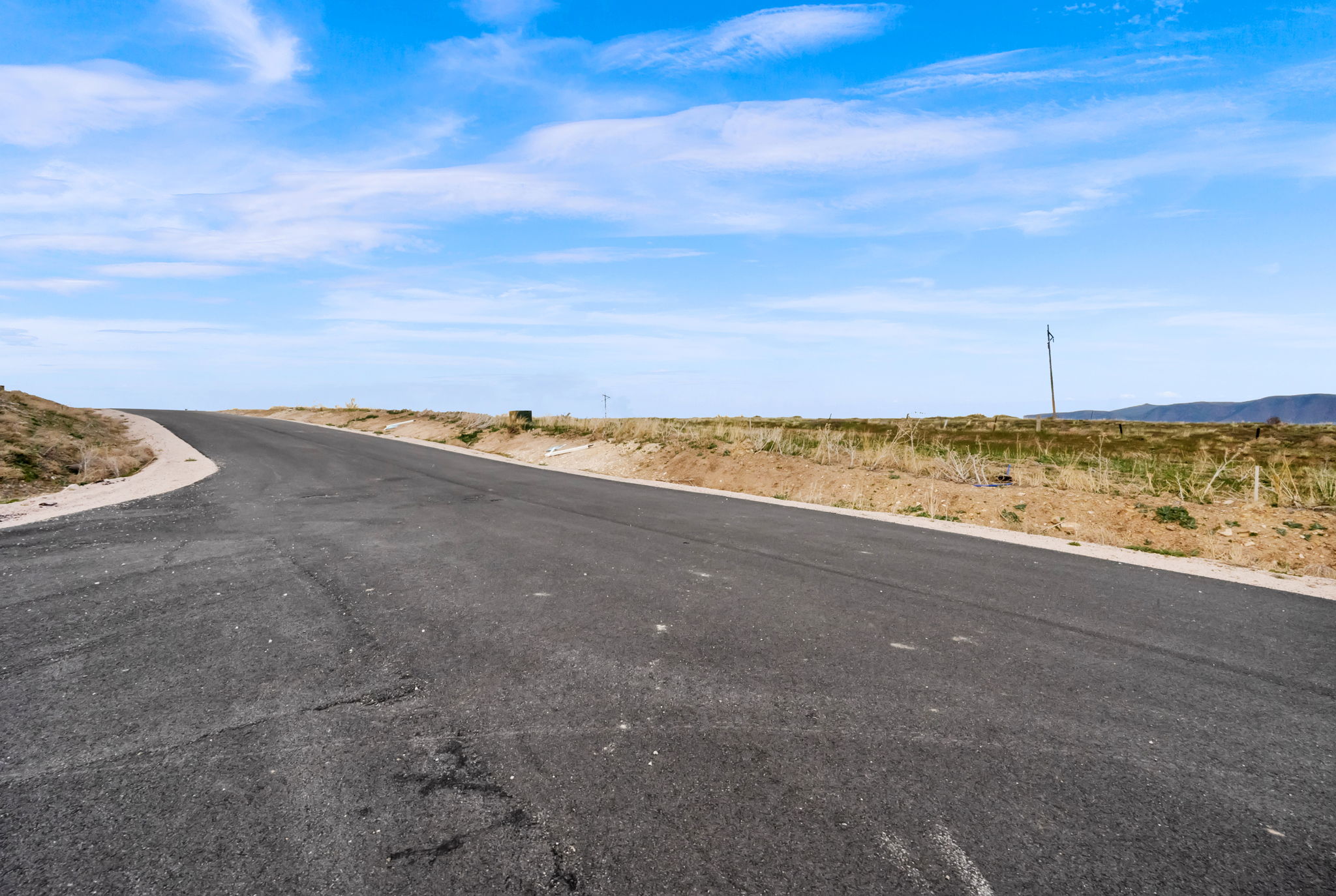 Paved road with a gradual incline, bordered by natural terrain