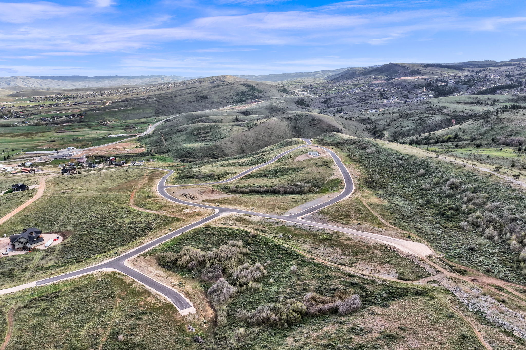 Expansive land featuring paved road infrastructure, rolling hillsides, and distant mountainous terrain