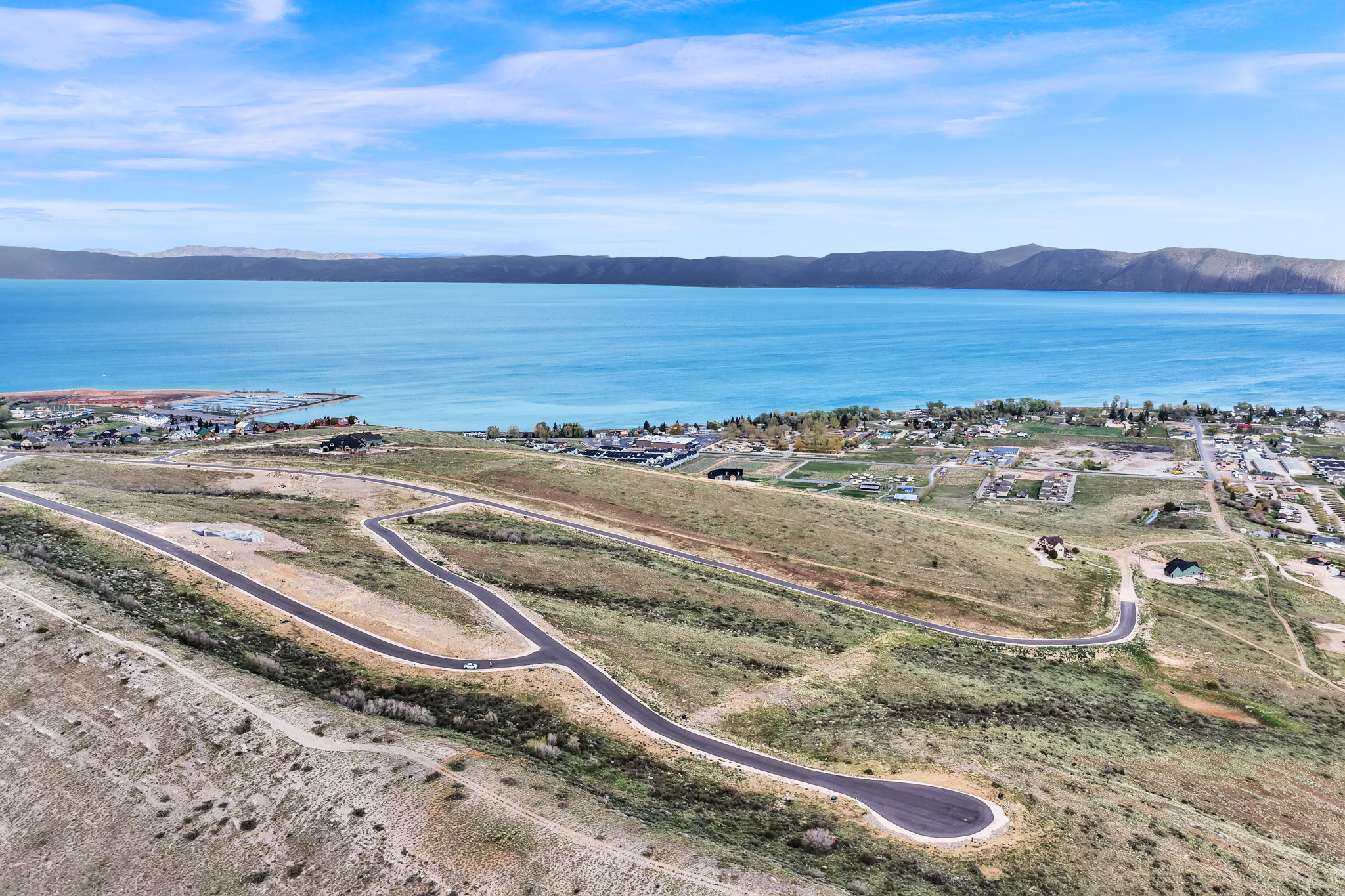 Expansive land parcel featuring paved roads, scattered residential structures, and a prominent water body