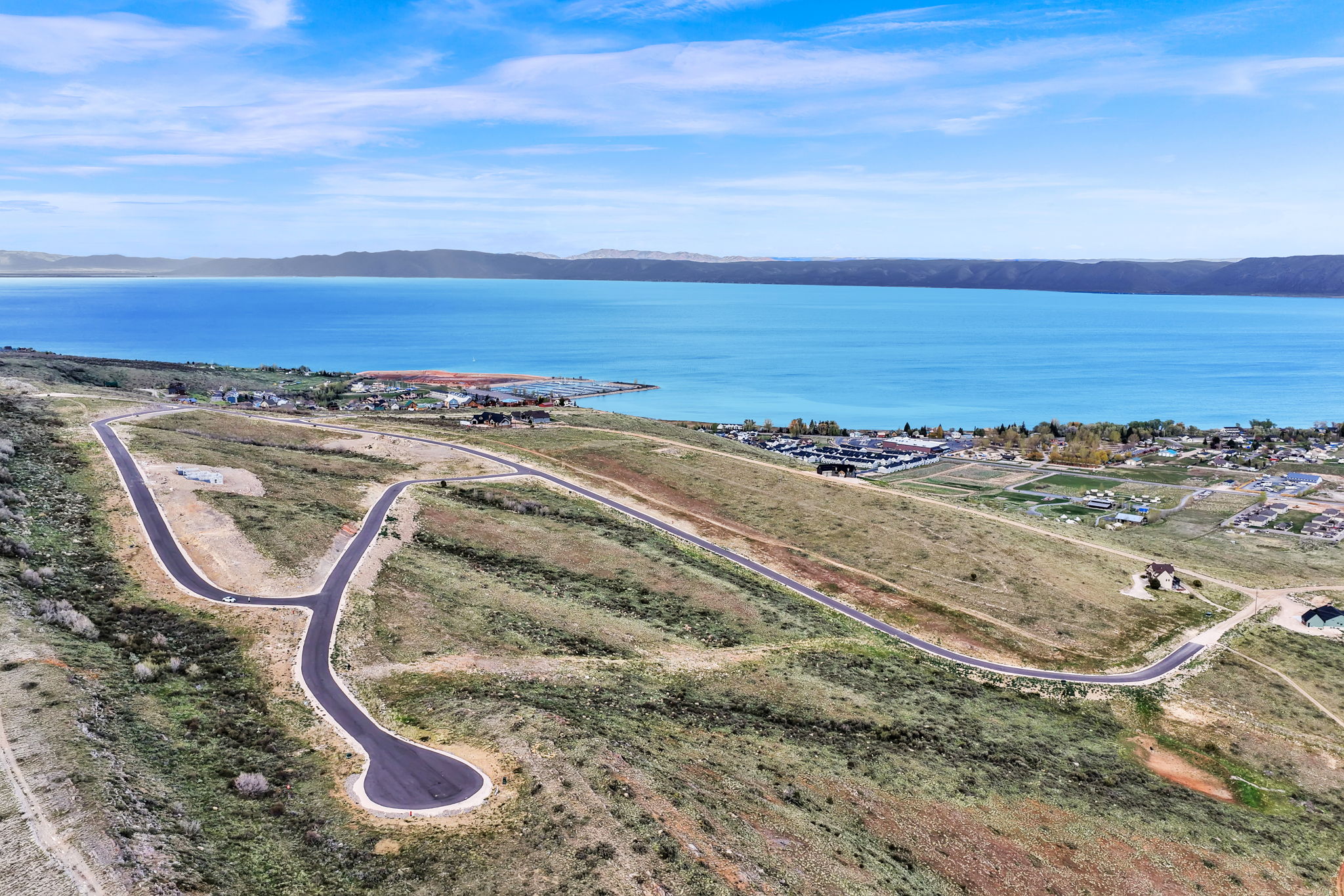 Expansive undeveloped land featuring a cul-de-sac and paved roads, set against a backdrop of a large body of water and distant mountains