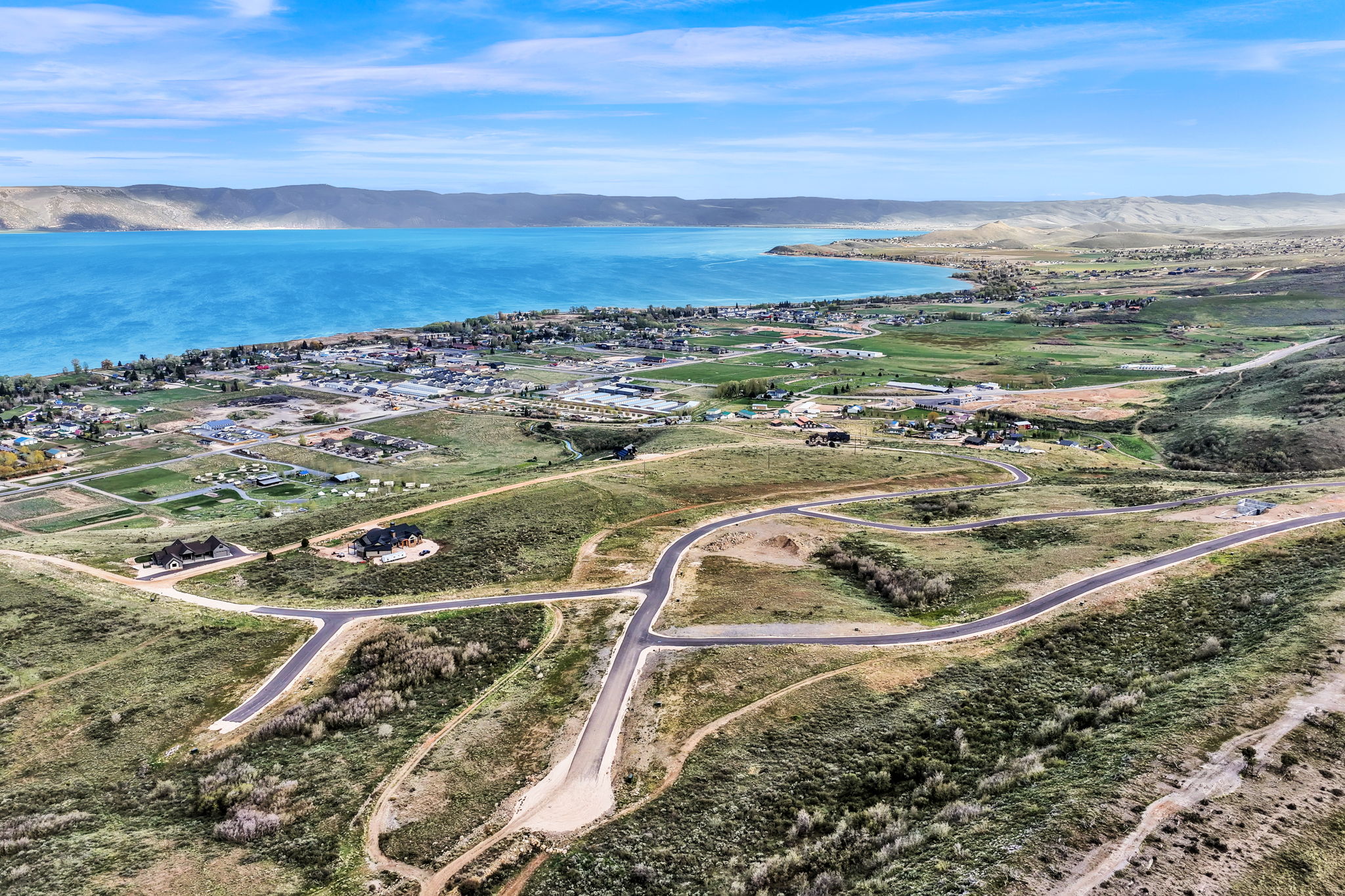 Expansive undeveloped land featuring paved roads, scattered mature trees, and direct access to a large body of water