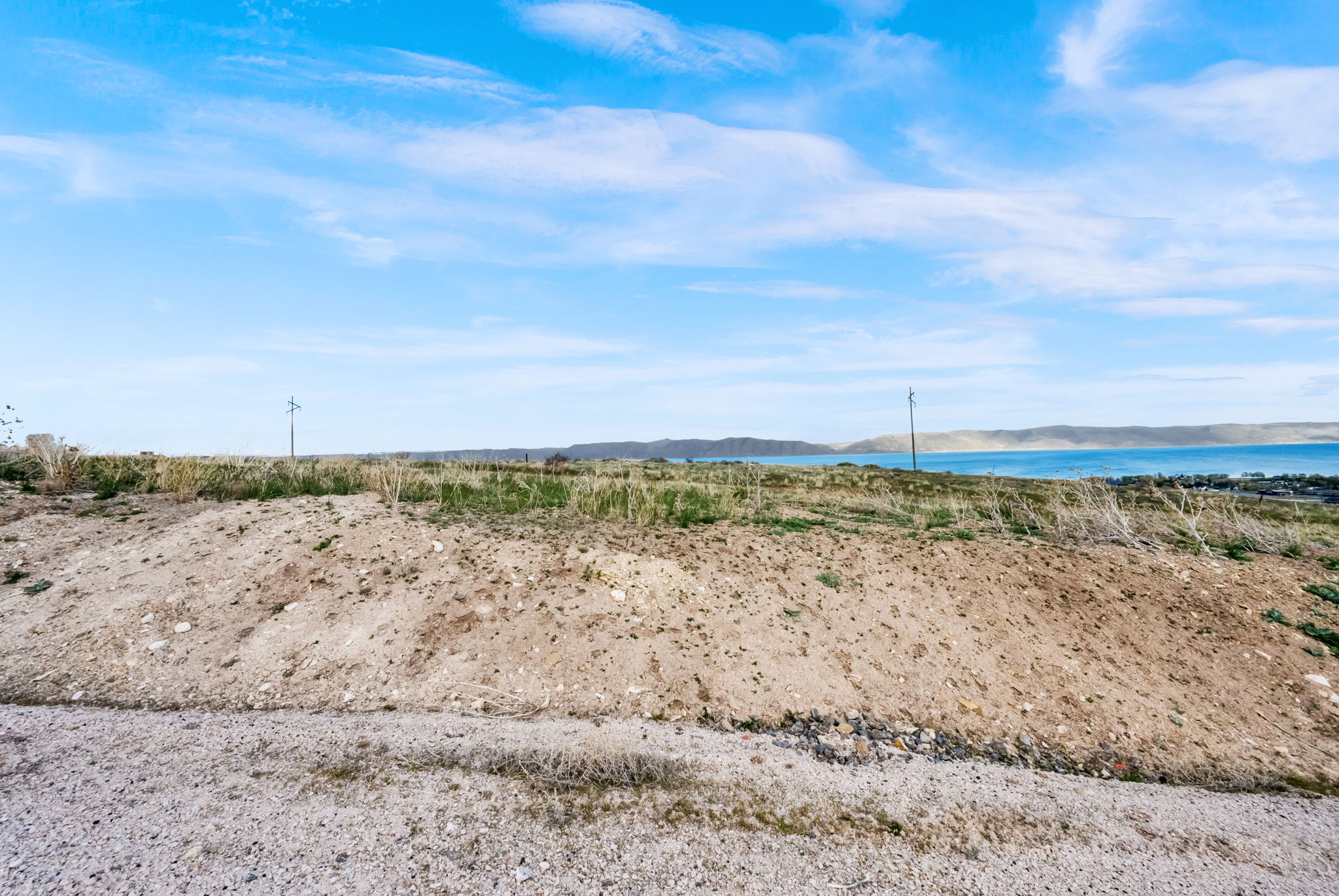 Expansive undeveloped land featuring a broad water body and distant hills under a vast blue sky