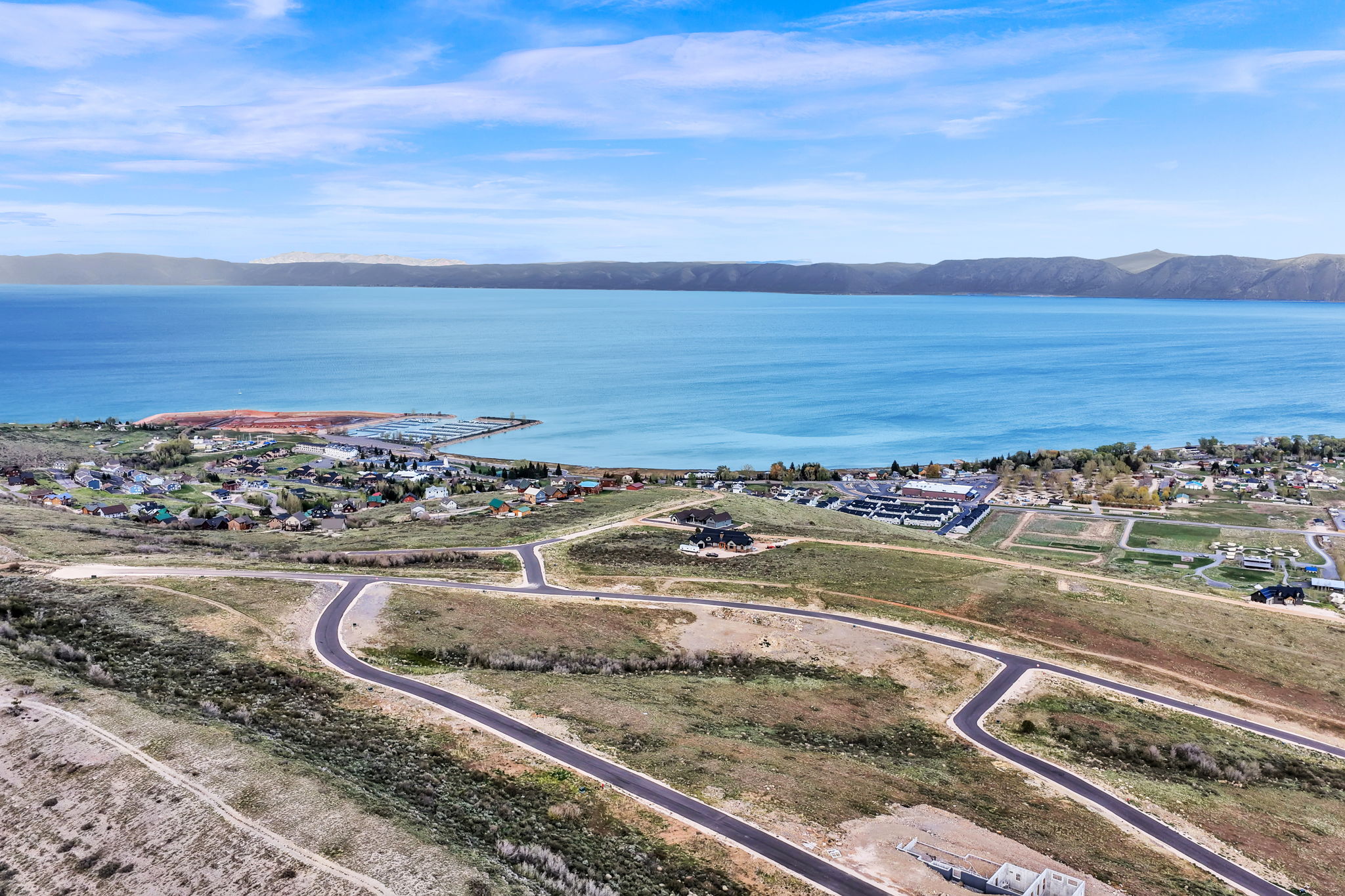 Expansive waterfront property featuring a deep blue lake, surrounding mountains, and paved roadways