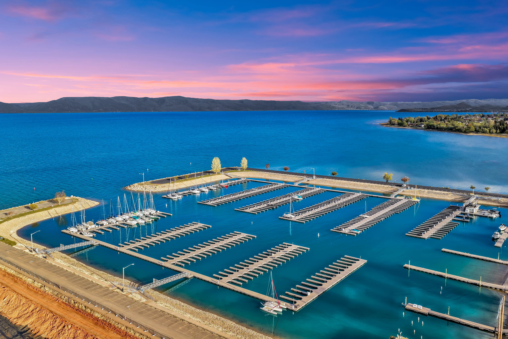 Expansive marina featuring multiple boat slips on vibrant blue waters, framed by distant hillsides and a colorful sky