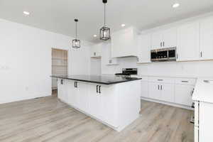 Kitchen featuring white cabinets, stainless steel appliances, hanging light fixtures, a kitchen island, and recessed lighting