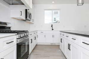 Kitchen with stainless steel appliances, white cabinetry, light wood-style floors, hanging light fixtures, and dark stone counters