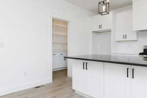 Kitchen with white cabinetry, dark stone counters, pendant lighting, light wood-style floors, and stainless steel range oven