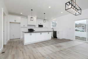 Kitchen with hanging light fixtures, white cabinets, a kitchen island, recessed lighting, and light wood-style flooring