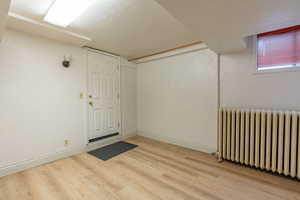 Finished below grade area featuring radiator heating unit, light wood-style flooring, and a textured ceiling