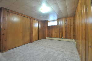 Below grade area featuring light carpet, wood walls, and a baseboard heating unit