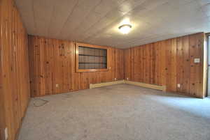 Unfurnished room with wooden walls, carpet floors, and baseboard heating