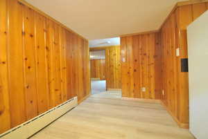 Hall featuring a baseboard radiator, wood finished floors, and wood walls