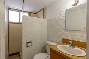 Full bath featuring vanity, tiled shower, and brick wall