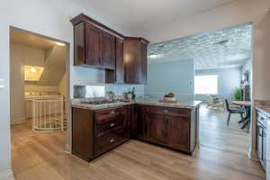Kitchen with dark brown cabinetry, light countertops, light wood finished floors, a peninsula, and washer and clothes dryer