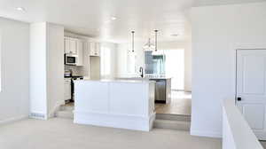 Kitchen featuring an island with sink, decorative light fixtures, stainless steel appliances, white cabinetry, and light colored carpet (pictures of home previously built)