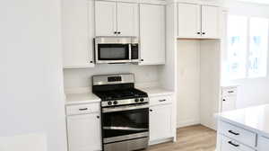 Kitchen featuring stainless steel appliances, white cabinetry, light wood finished floors, and light stone countertops (pictures of home previously built)